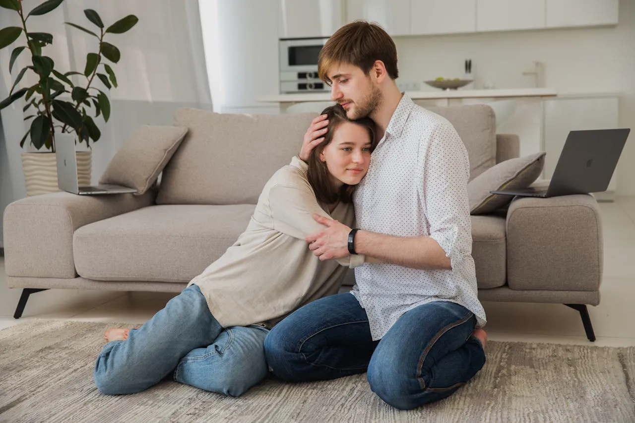 A young couple sitting together on the floor, the partner gently holding her as they navigate an important moment together.